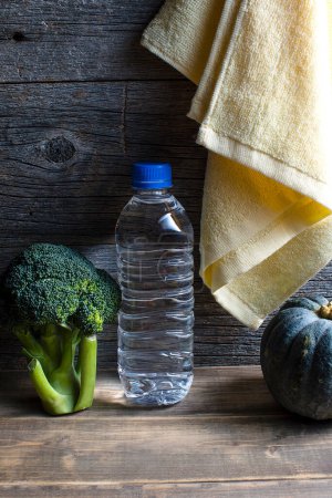 Foto de Estilo de vida saludable. Botella de agua, toalla, brócoli y calabaza sobre fondo de madera - Imagen libre de derechos