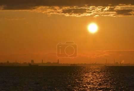 Foto de Hermosa puesta de sol sobre el mar y el horizonte de la ciudad. El Sol brilla a través de las nubes. - Imagen libre de derechos