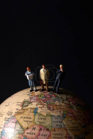 Foto de Figuras de personas en miniatura de pie en la parte superior del modelo de globo terráqueo sobre fondo negro - Imagen libre de derechos