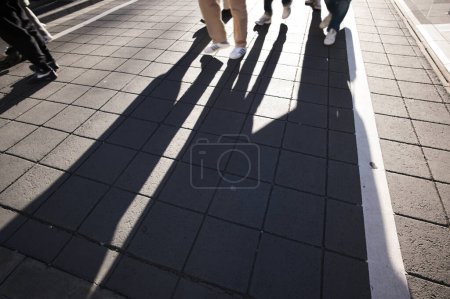 Photo for Long shadows of pedestrians walking down the street at sunset - Royalty Free Image
