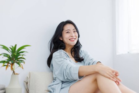 Téléchargez les photos : Belle femme asiatique avec de longs cheveux noirs assis sur le lit après le réveil - en image libre de droit