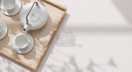 Téléchargez les photos : Vue de dessus de moderne, minimale, belle théière en céramique blanche, tasse de thé avec soucoupe sur plateau en bois mat de paille marron sur nappe crème à la lumière du soleil, ombre à feuilles avec fond d'espace 3D - en image libre de droit