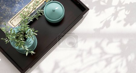 Photo for Dark wooden serving tray, ceramic turquoise blue vase and jar and antique blue Chinese book with space on white fabric tablecloth table in sunlight, leaf shadow for interior design decoration 3D - Royalty Free Image