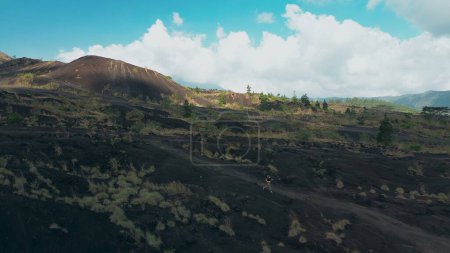 Téléchargez les photos : Vue aérienne d'une jeune belle femme courant sur la lave volcanique noire dans les montagnes. Mode de vie sain et désir d'explorer le monde. Jogging en montagne, vêtements sportifs. - en image libre de droit