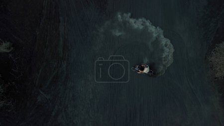 Téléchargez les photos : Un jeune homme dérive sur une moto sur de la lave volcanique noire, vue de dessus. Dérive sur le sable volcanique, des nuages de sable s'élèvent. Des cascades spectaculaires sur un moteur dans le sable. - en image libre de droit