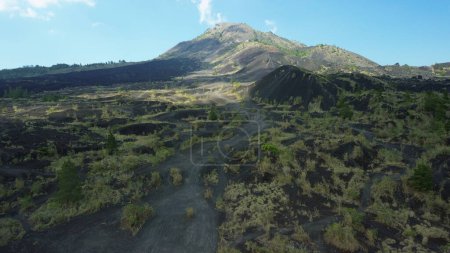 Photo for Shooting from a drone from a birds eye view of the Batur volcano in Bali. Black lava and motorcycle tracks from above on the volcano. Mountain trails for climbing, a beautiful view of the mountains. - Royalty Free Image