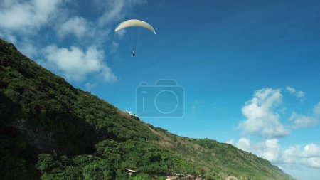 Photo for Bottom view of a pair of glider pilots flying on a paraglider, a tourist, and an instructor. White paraglider against a green hill and blue sky. Sports and extreme lifestyle. - Royalty Free Image