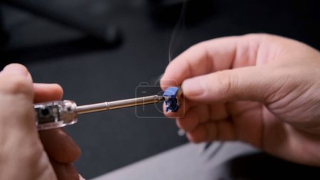 Foto de Un ingeniero conecta dos partes de un circuito de radio con un soldador. Primer plano de las manos masculinas que trabajan con un soldador. - Imagen libre de derechos