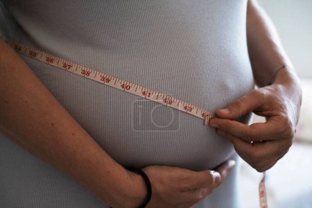 Photo for Close-up of a pregnant womans big belly, measuring her belly with an inch tape. Weight gain during pregnancy, monitoring the health of a pregnant woman. - Royalty Free Image