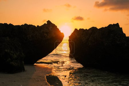 Photo for Beach with rocks during sunset, golden hour. Setting sun between the rocks of the beach, picturesque view. Background photo with sunset, natural background for design. Picturesque tropical landscape. - Royalty Free Image
