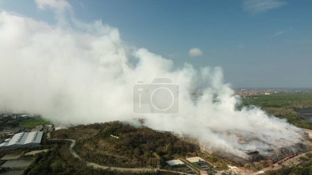 Photo for A powerful fire at the largest landfill on the island of Bali. The fire is being extinguished by many fire engines and helicopters. A huge column of smoke from the fire spreads to neighboring areas. - Royalty Free Image