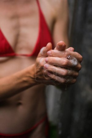 Téléchargez les photos : Une jeune belle femme en bikini rouge prend une douche tropicale à l'extérieur. Soins du corps et de beauté dans les climats tropicaux chauds. Mousse de gel douche, mousser les mains. - en image libre de droit