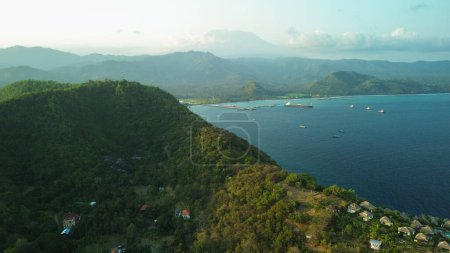 Foto de Vista aérea de una colina iluminada por la luz dorada del atardecer en el puerto de Padang Bai en la isla tropical de Bali. Vista de los barcos hundidos y el hotel donde los turistas se relajan. - Imagen libre de derechos