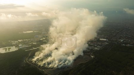 Foto de Vista aérea de un incendio de largo alcance en un vertedero grande con basura. Una espesa nube de humo tóxico se eleva en el aire. Problema con la contaminación atmosférica y el reciclaje de residuos. La basura se está quemando. - Imagen libre de derechos