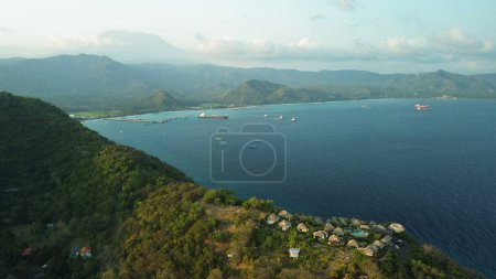 Photo for A picturesque birds eye view of the hill. Sunset time by the ocean, abandoned ships in the port and the ocean. Located on a hill is a hotel for your Bali holiday. - Royalty Free Image