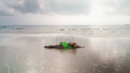 Foto de Sexy mujer afroamericana de talla grande tumbada en la playa en un traje de baño verde. El concepto de descanso y relajación en un país tropical. Positividad corporal y amor propio. - Imagen libre de derechos