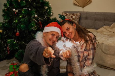 Photo for Family traditions and celebration of Christmas and New Year. A Christmas family with sparklers against the background of a Christmas tree. - Royalty Free Image