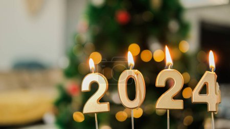 Foto de Fondo de Año Nuevo con velas doradas encendidas con el número 2024 en el fondo de un hermoso bokeh de un árbol de Navidad con decoraciones y guirnaldas. - Imagen libre de derechos