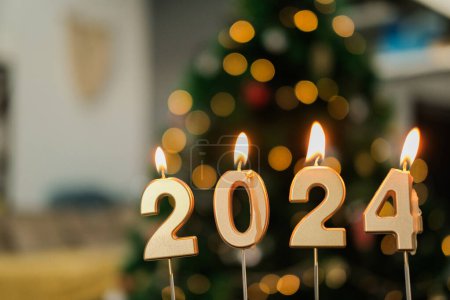 Foto de Fondo para una bandera de Año Nuevo con velas en forma de números 2024 en color oro. Las velas están ardiendo y la cera fluye a través de ellas. Un árbol de Navidad con guirnalda resplandece en el fondo. - Imagen libre de derechos