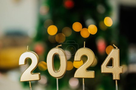 Foto de Velas con números dorados 2024 en el fondo de un árbol de Navidad con guirnalda y decoraciones, hermoso bokeh. Tarjeta de Año Nuevo 2024 como regalo. En la víspera de Navidad. - Imagen libre de derechos