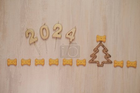 Téléchargez les photos : Fond du Nouvel An sur une planche en bois avec des biscuits pour chiens en forme d'os et de bougies avec les numéros 2024 disposés. A proximité se trouve un jouet brillant pour l'arbre de Noël. - en image libre de droit