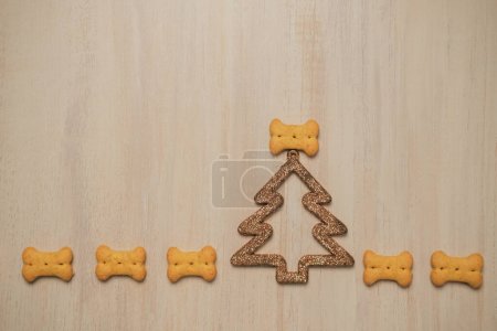 Téléchargez les photos : Vue de dessus des biscuits pour chiens en forme d'os qui sont disposés sur une planche de bois à côté d'un sapin de Noël brillant. Contexte pour un animalerie. Bannière avec friandises pour chiens dans le concept du Nouvel An. - en image libre de droit