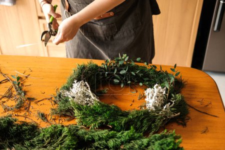 Photo for A young woman with wire cutters in her hands cuts branches from a spruce tree to make a Christmas wreath. Workshop on making decorations for Christmas and New Year. - Royalty Free Image