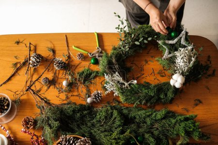 Photo for Banner with making a Christmas wreath from fir branches. The hands of a young woman above the table collect a wreath and decorate it with cones and balls. DIY decorations for the New Year. - Royalty Free Image