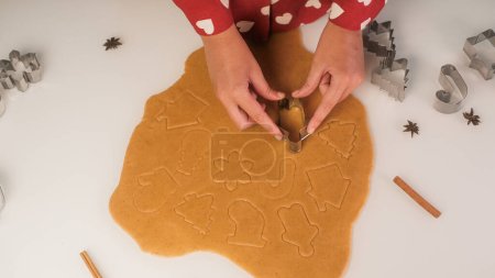 Foto de Vista superior de una mesa con galletas de jengibre hechas por una mujer joven. Cortadores de galletas y masa en la mesa. Hombre de jengibre, árbol de Navidad y copo de nieve. - Imagen libre de derechos