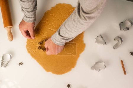 Photo for Top view of a table with gingerbread cookies being made by men. Cookie cutters and dough on the table. Gingerbread man, Christmas tree and snowflake. - Royalty Free Image