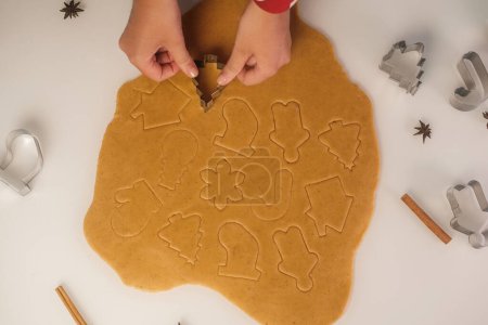 Foto de El proceso de preparación de pan de jengibre de Navidad para una cena de vacaciones. Una joven en pijama rojo con corazón prepara galletas de jengibre en la cocina. - Imagen libre de derechos