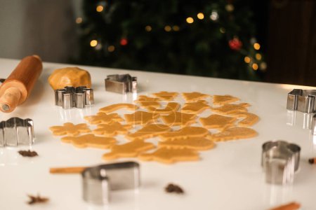 Foto de Fondo de panadería. En una mesa blanca se extiende la masa sobre la que se exprimen las galletas de jengibre en forma de copos de nieve, un muñeco de nieve y un hombre de jengibre utilizando moldes. Hornear Navidad. - Imagen libre de derechos