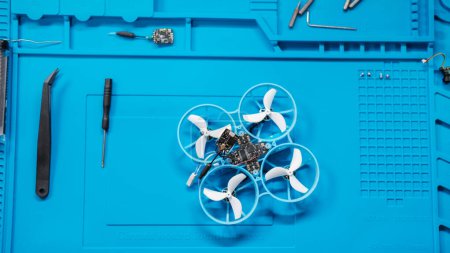 Téléchargez les photos : Vue du dessus du bureau dans le service de réparation de drones FPV. Sur la table se trouve un drone démonté, avec des micropuces, un fer à souder et d'autres outils. Un ingénieur prépare un drone pour le vol. - en image libre de droit