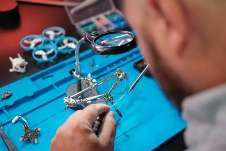 Photo for Close-up of a male engineers hands soldering a video transmitter chip from an FPV drone using a magnifying glass. Service center for repair and maintenance of equipment. Drone repair. - Royalty Free Image