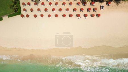Foto de Vista superior de un club de playa con tumbonas y sombrillas rojas en la orilla del océano de arena blanca. Playa de arena blanca, corales, agua turquesa y un lujoso club en la costa de Bali. - Imagen libre de derechos