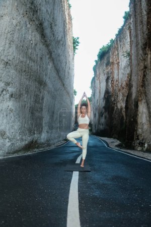 Foto de Una joven hermosa latina con el pelo rizado realiza una pose de yoga asana en un desfiladero entre dos grandes rocas blancas. Clases de yoga al aire libre en la naturaleza. Actividades de bienestar. - Imagen libre de derechos