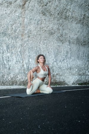 Foto de Una joven latina hermosa con el pelo rizado realiza una asana de yoga sobre el fondo de una roca blanca. Clases de yoga en la naturaleza. Banner para yoga y centro de retiro. Centro de bienestar. - Imagen libre de derechos