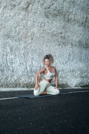 Foto de Una joven latina hermosa con el pelo rizado realiza una asana de yoga sobre el fondo de una roca blanca. Clases de yoga en la naturaleza. Banner para yoga y centro de retiro. Centro de bienestar. - Imagen libre de derechos