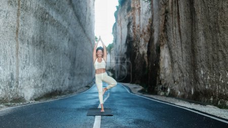 Foto de Una joven hermosa latina con el pelo rizado realiza una pose de yoga asana en un desfiladero entre dos grandes rocas blancas. Clases de yoga al aire libre en la naturaleza. Actividades de bienestar. - Imagen libre de derechos