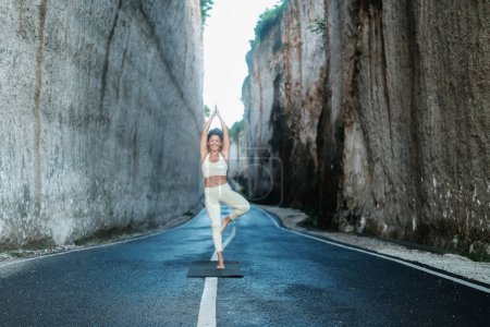 Téléchargez les photos : Une jeune belle femme latine aux cheveux bouclés effectue une pose d'arbre yoga asana dans une gorge entre deux grandes roches blanches. Cours de yoga en plein air dans la nature. Activités bien-être. - en image libre de droit