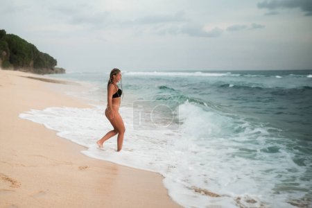 Foto de Sexy bikini cuerpo joven latina mujer con trenzas juguetona en el paraíso tropical playa divertirse jugando salpicaduras de agua en libertad. Hermosa mujer en forma de cuerpo en vacaciones de viaje Banner cultivo para el espacio de copia - Imagen libre de derechos