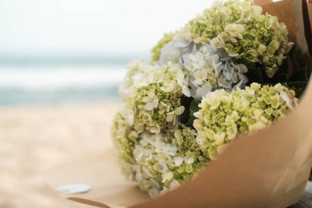 Téléchargez les photos : Gros plan d'un bouquet d'hortensias bleues blanches et jaunes qui se trouve sur le sable de la plage près de l'océan. Bouquet de mariage pendant la cérémonie. Bannière avec hortensias pour un salon de fleurs. - en image libre de droit