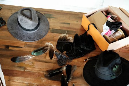 Foto de Vista superior de una mesa de madera de un sombrerero de mujer que decora un sombrero gris con plumas, hilos y retazos de tela. El proceso de creación de un tocado y el espacio de trabajo de un diseñador de moda. - Imagen libre de derechos