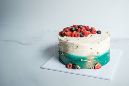 Photo for Banner with a cake, which is covered with turquoise and white cream, decorated with fresh berries. It is located on a stand in the production area of the confectionery. Beautiful birthday cake. - Royalty Free Image
