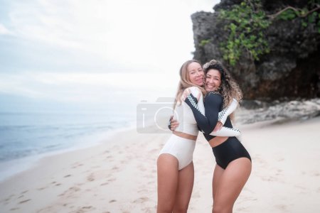 Foto de Dos jóvenes y diversas mujeres sexy en bikini de surf blanco y negro abrazándose en la playa y sonriendo. Amistad femenina en la comunidad de surf. Comunicación con personas afines. - Imagen libre de derechos
