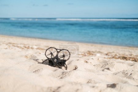 Téléchargez les photos : Sur la plage près de l'océan, il y a un drone FPV couché sur le sable, qui a perdu son signal et est tombé. Le drone aérien est cassé. Restauration et réparation de l'électronique. - en image libre de droit