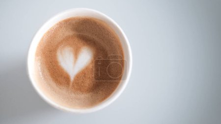 Téléchargez les photos : Une bannière avec une tasse écologique recyclable jetable dans laquelle du café cappuccino chaud avec de la mousse et un motif de coeur est versé. Café avec du lait d'avoine alternatif. Une tasse matinale de boisson revigorante. - en image libre de droit