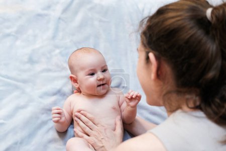 Photo for Top view of a baby lying on a blanket in a white diaper and his mother looking at him with love and affection. Little newborn girl laughs and experiences positive emotions. Mothers Day. - Royalty Free Image