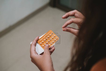 Close up of a hands young woman holding a package of birth control pills. She takes out one pill and takes it. Contraceptives and birth control. Childfree people.