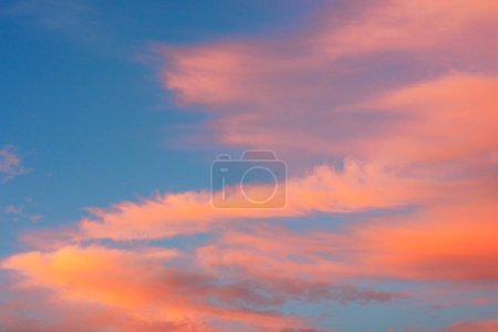 Photo for Long wispy orange cirrus clouds streamers during sunset golden hour against blue sky - Royalty Free Image